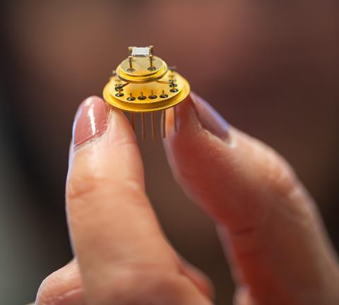 Close up of an 'electronic nose' - small electronic circuitry on gold-coloured metal - held in someone's fingertips