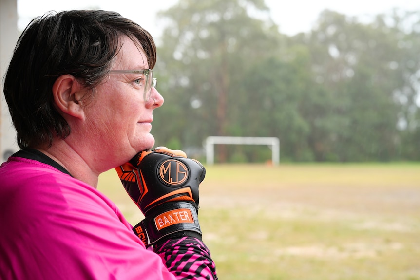 a white woman with short dark hair and glasses looking sideways out to a soccer field
