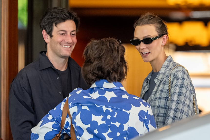 A man and a woman speak with another woman whose face is not shown.
