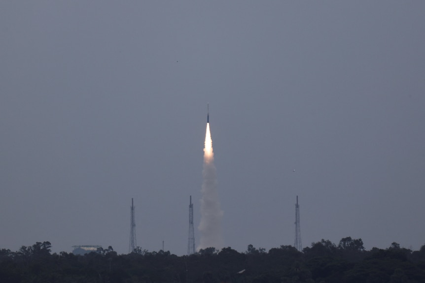 A tall, thin rocket blasts vertically into the sky, leaving a trail of bright flames and grey smoke.