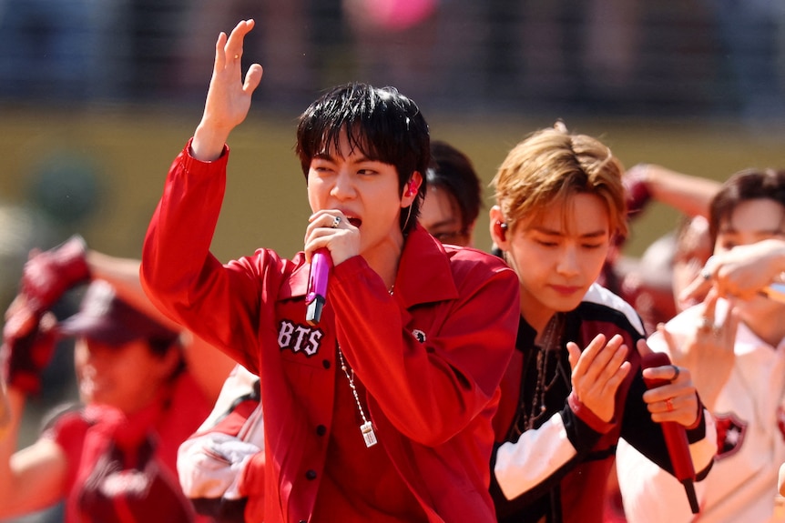 BTS members holding mics, singing and dancing on stage