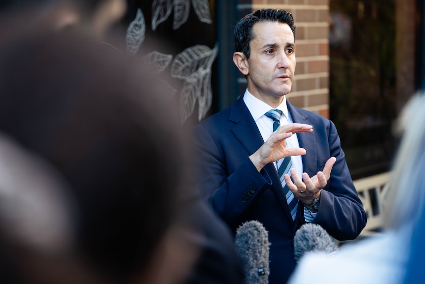 A man in a blue suit watching someone speak at a press conference.