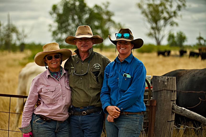 A farming family smiling for a photo against a fence on a farm.