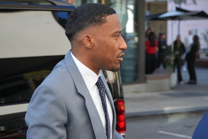 A close-up, side-on shot of Yung Filly wearing a grey suit, white shirt and dark tie in the Perth CBD.