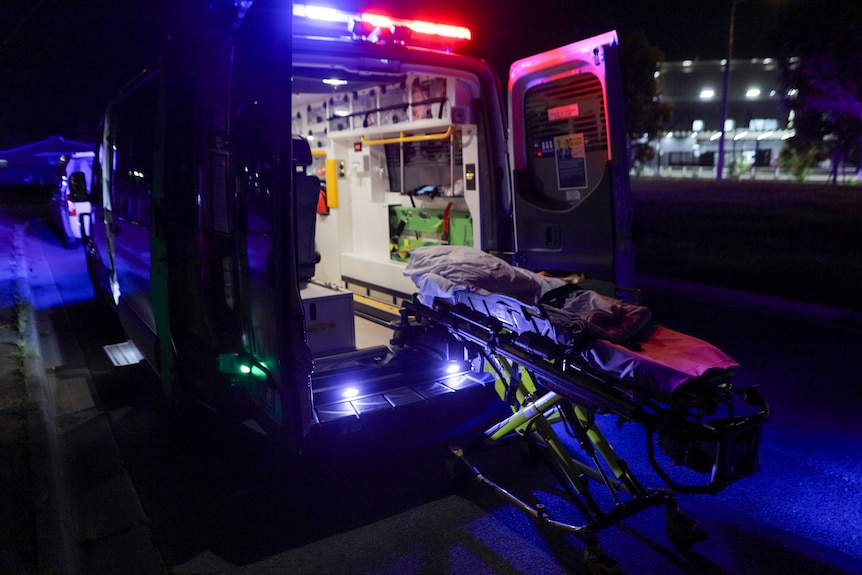 A stretcher bed rests outside the open doors of the back of an ambulance.