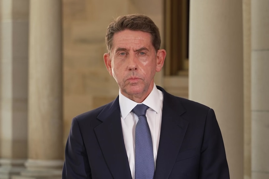 A man in a suit looking into camera in front of sandstone background.