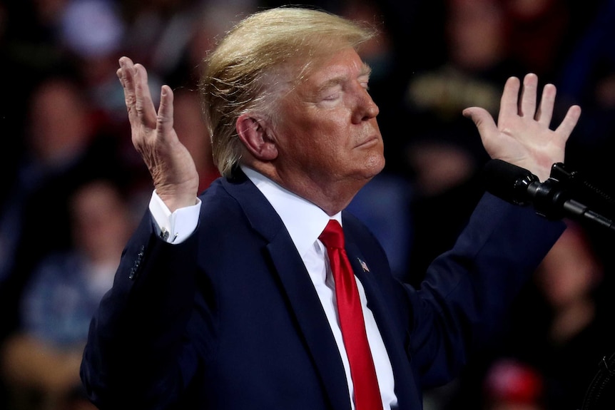 Donald Trump raises both hands in the air, his eyes closed.