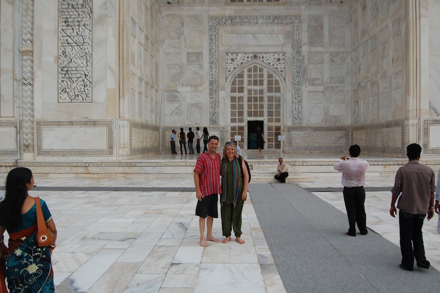 A couple stand barefoot at a white-tiled Indian monument