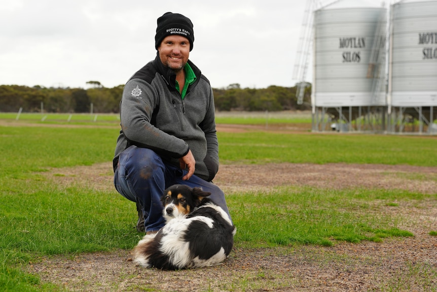 A farmer and his dog in front of a grain silo