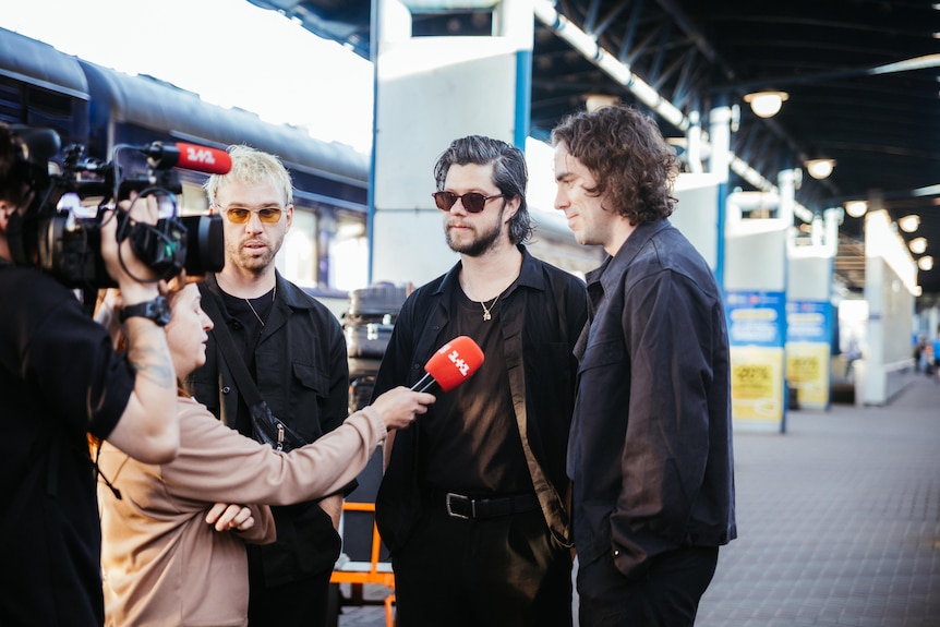 Three men are interviewed by a television crew.