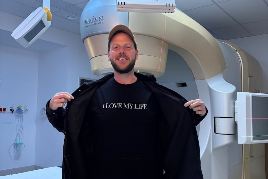 A young man with a cap in a hospital setting wears a black shirt that says "I love life".