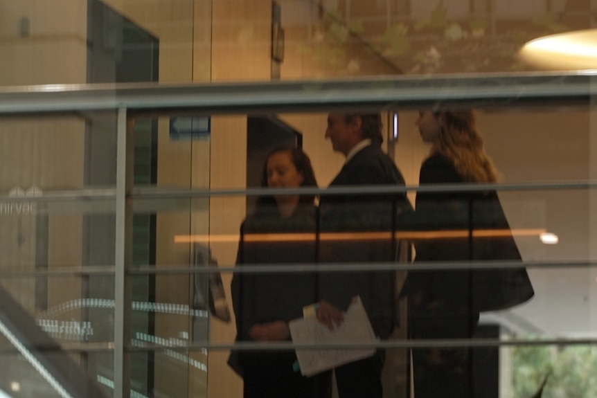 Three people waiting to enter a lift.