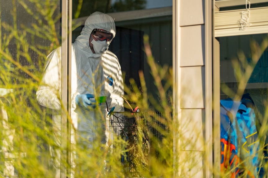 A man in full protective gear inside a house holding a container next to a cage.