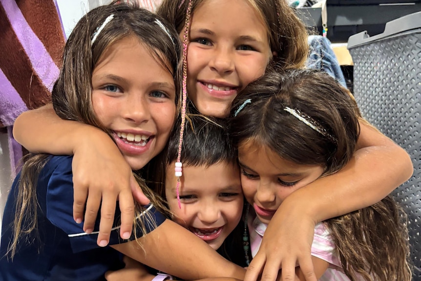 Four children huddled in a group hug, smiling for a photo