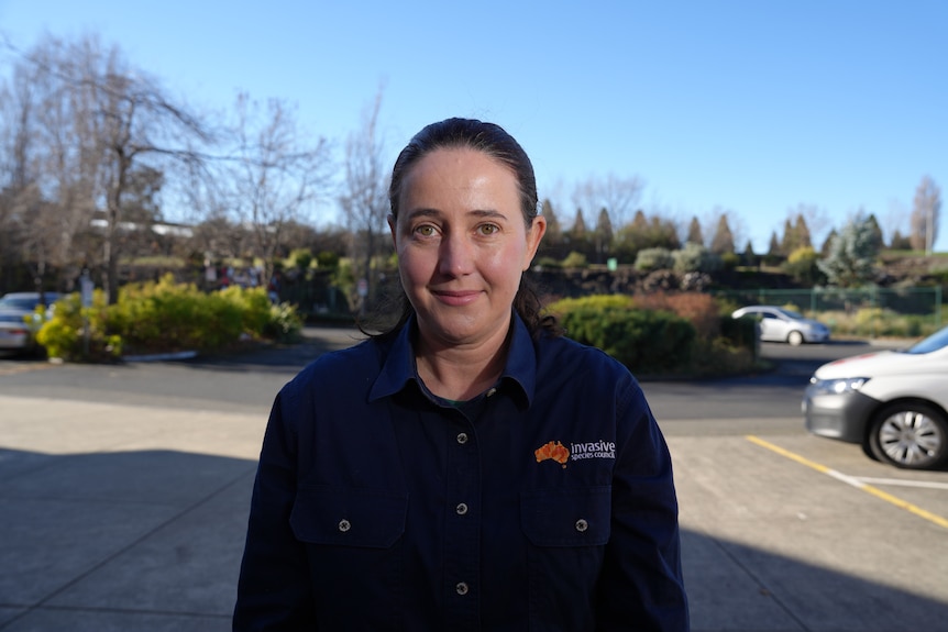 A woman with brown hair tied back in a navy shirt with the invasive species council logo smiles while standing in a carpark.