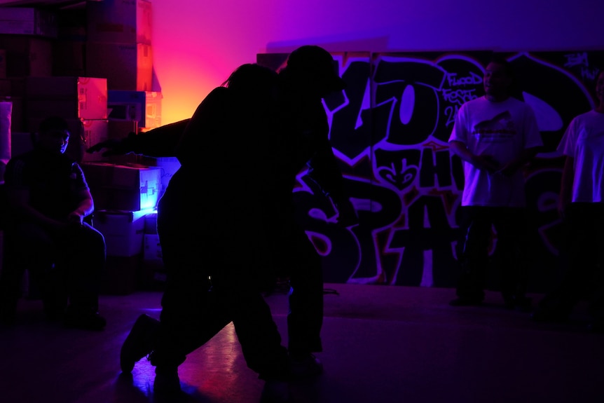 Two people dance in silhouette moving in a small room lit by red and blue strobe lights.