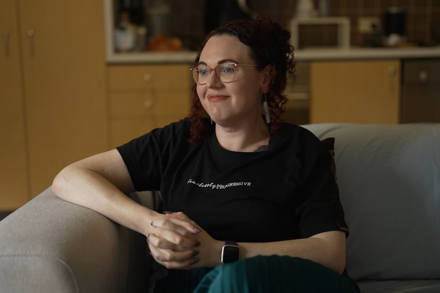 A woman wearing a black shirt sitting on the corner of a couch.