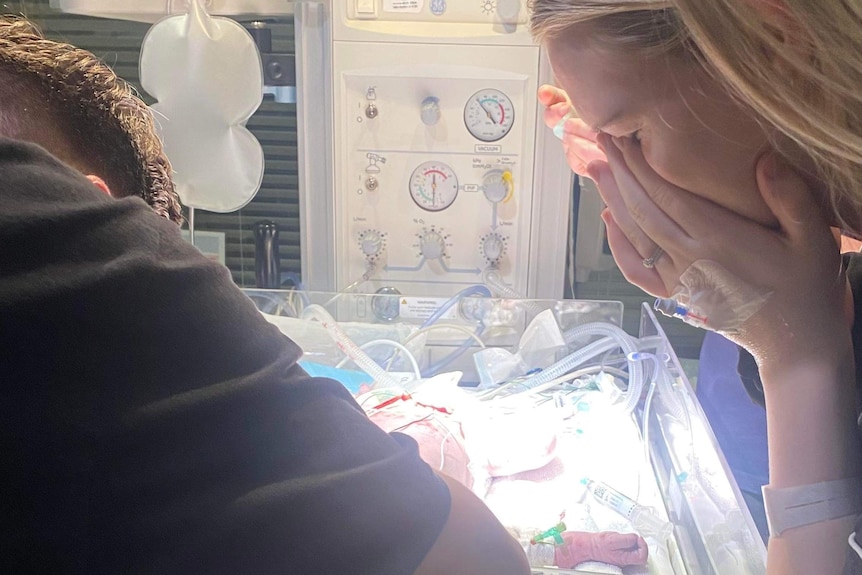 Meg and James lean over a crib, looking at baby Thea inside