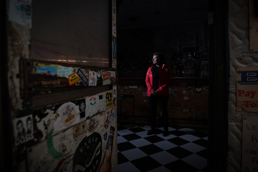 A wide shot taken through a hotel's front door shows a woman standing inside the pub, the photo is dark and eerie.