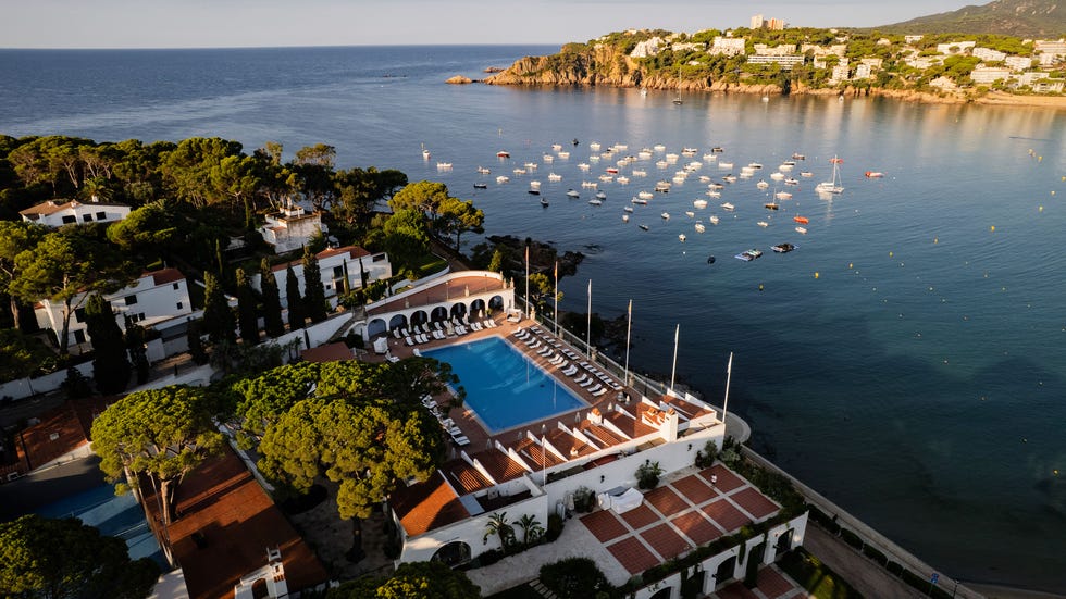 aerial view of a coastal resort with a large pool and docked boats in the bay.