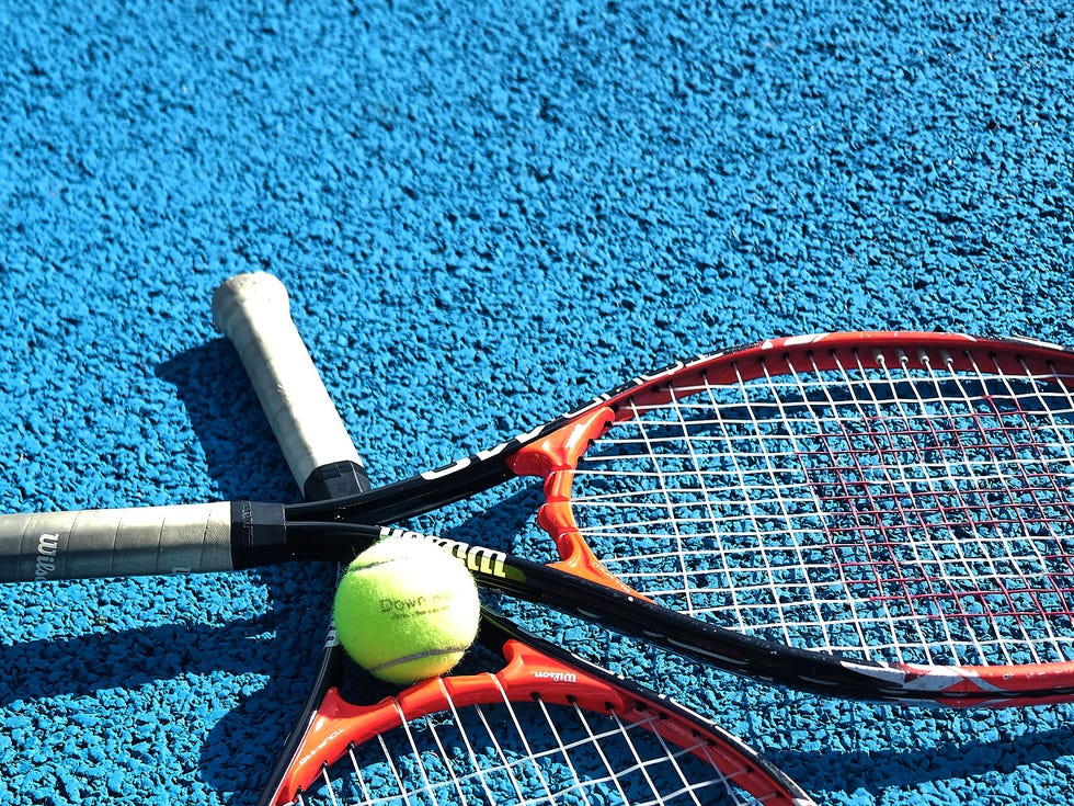 Down Hall two tennis rackets and a ball on blue court.