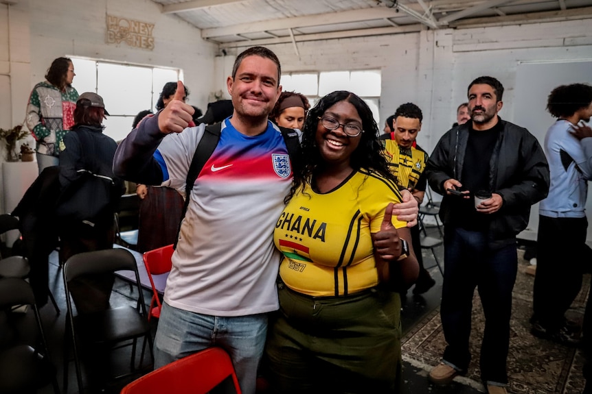 A man wearing a blue, white and red football jersey stands with his arm around a woman wearing a yellow jersey with GHANA on 