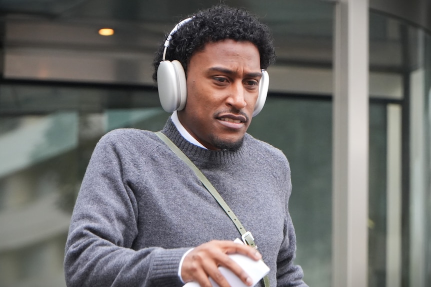 Yung Filly wears grey jumper and headphones while walking out of the District Court.