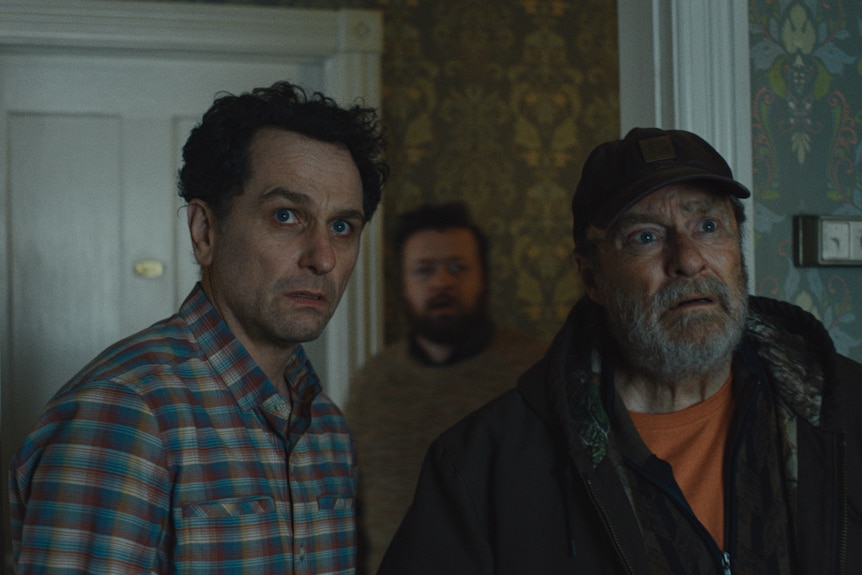 Two men stand in a doorway while a third man stands behind them.