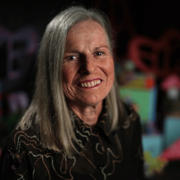 Virginia Lumsden headshot. A woman with blonde/grey hair smiles. She wears a dark-coloured top with a high neckline