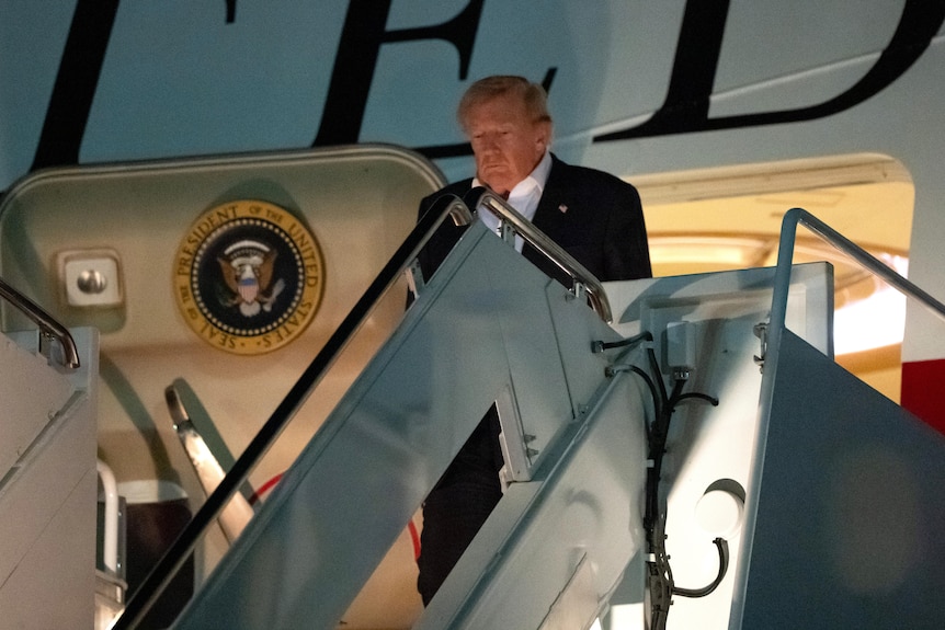 Donald Trump looks down as he stands at the top of the stairs of a jet plane