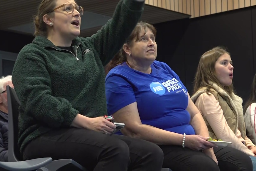 A woman in a green jumper pointing off-screen while another woman in a blue t-shirt looks the same way