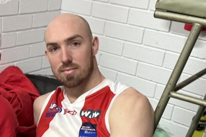 Grady man with a beard sitting in an AFL locker room.