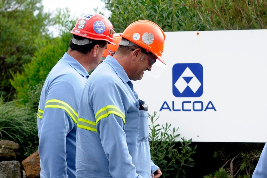 Two workers walk past the Alcoa logo.