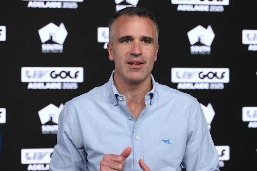 A man wearing a light blue shirt standing in front of a banner with LIV GOLF logos on it