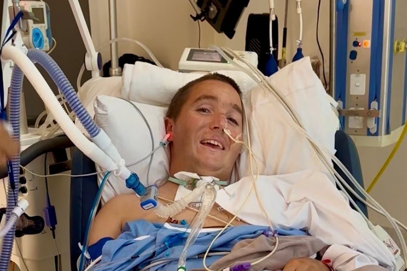 A man in a hospital bed, with a recently installed tracheostomy tube