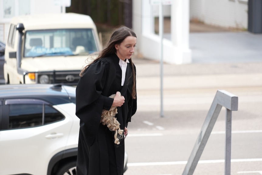 Woman in barrister gown holding white wig walking