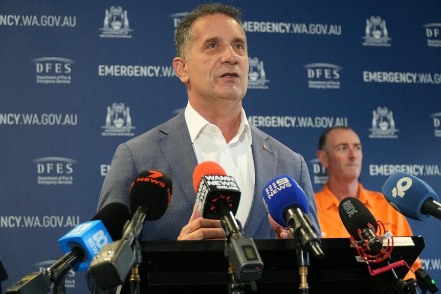 A man speaks to reporters standing infront of the logo of the Department of Fire and Emergency Services