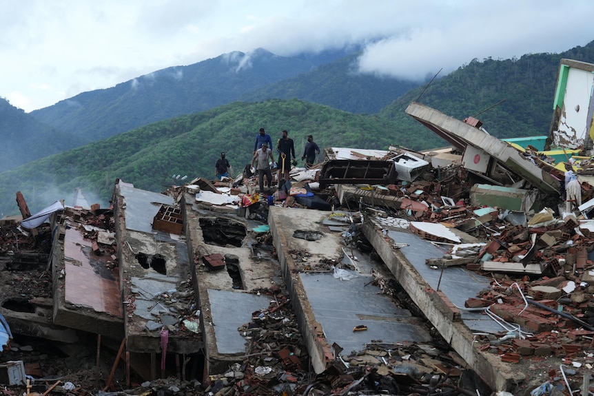 The silhouettes of five people standing on slanted collapsed roofs of buildings and a mountain of rubble.