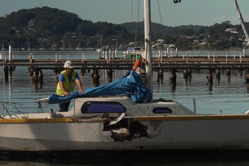 Two men standing on a small boat with a large hole in its side.