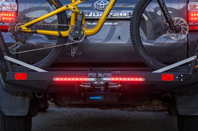 A yellow mountain bike secured to the rear of a vehicle with visible brake lights and a cargo rack. A yellow mountain bike secured to the rear of a vehicle with visible brake lights and a cargo rack.
