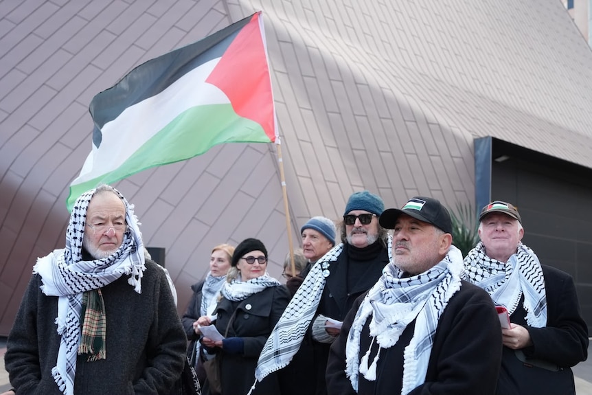Protesters dressed in black with keffiyehs, holding a Palestinian flag