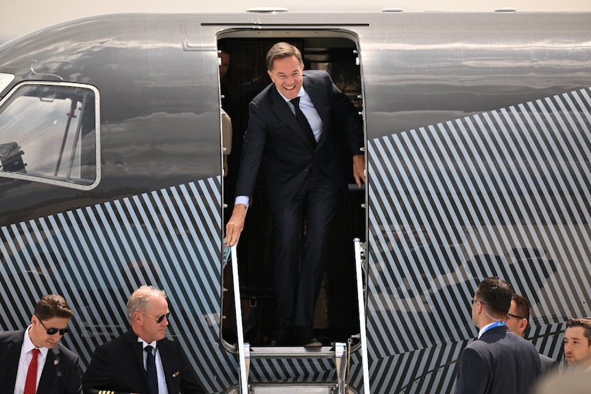 A man in a suit leaves an aircraft and smiles.
