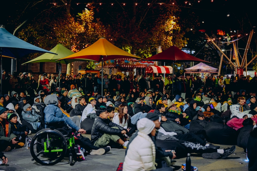 A group of people, some in Australian jerseys, at outdoor night-time viewing party