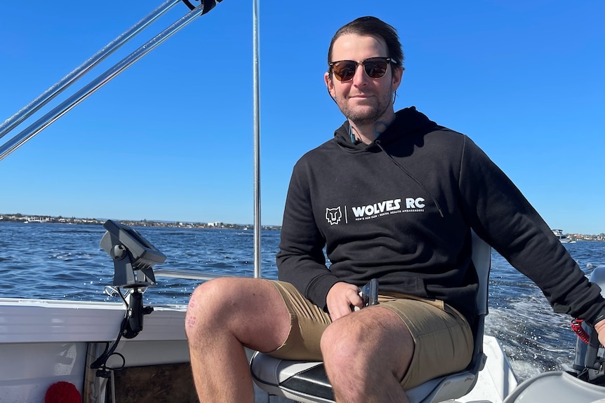 Laurence wears sunglasses as he smiles while sitting in a boat