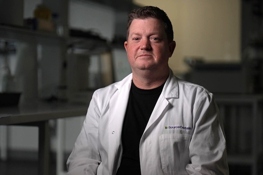 A white man wearing a lab coat over a black T-shirt.