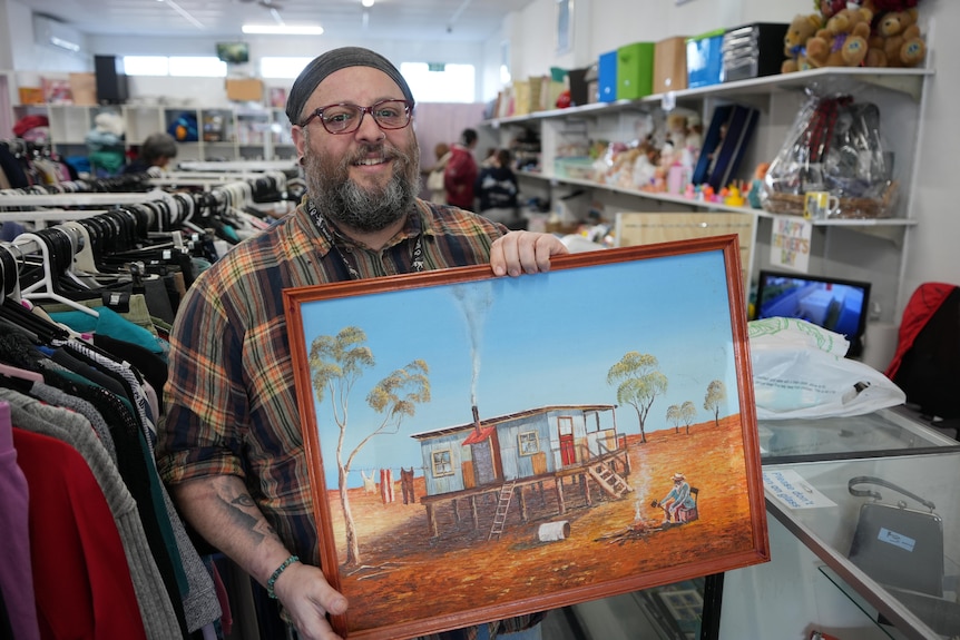 Man in checked shirt holding painting.