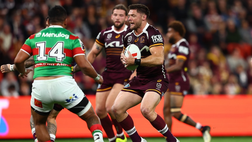 A Brisbane Broncos NRL player runs and braces in advance of a tackle against South Sydney.