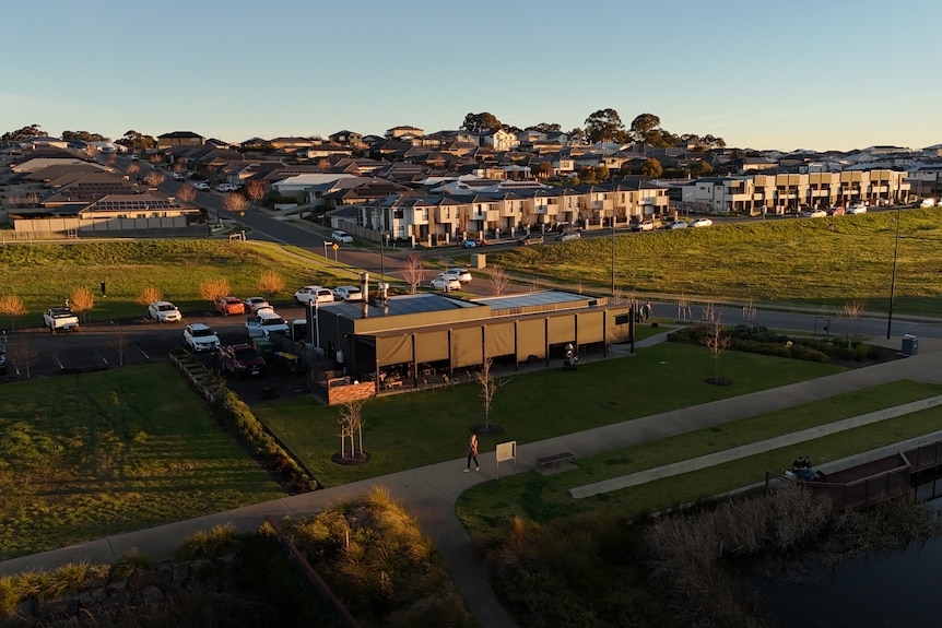 An aerial view of a building and carpark surrounded by a dam, three paddocks and then housing estates in the distance.