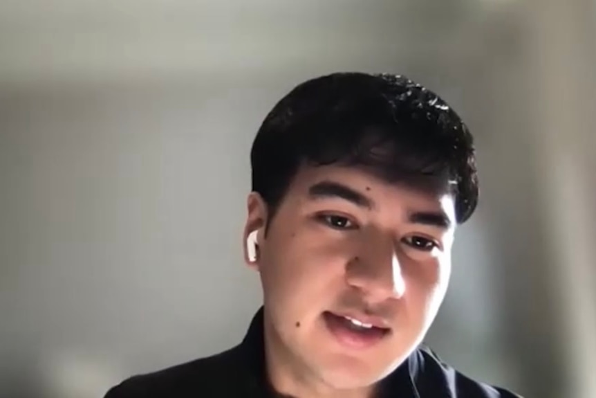 A young man with black hair, black shirt and earbud.