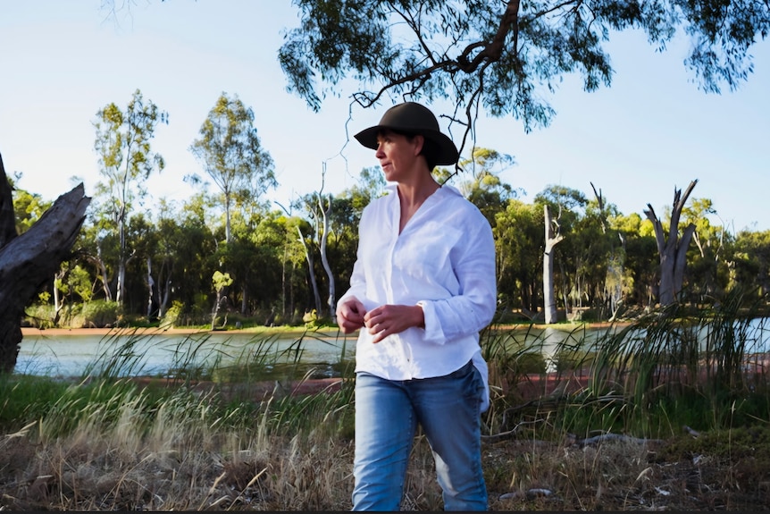 Jodie stands under trees by the water
